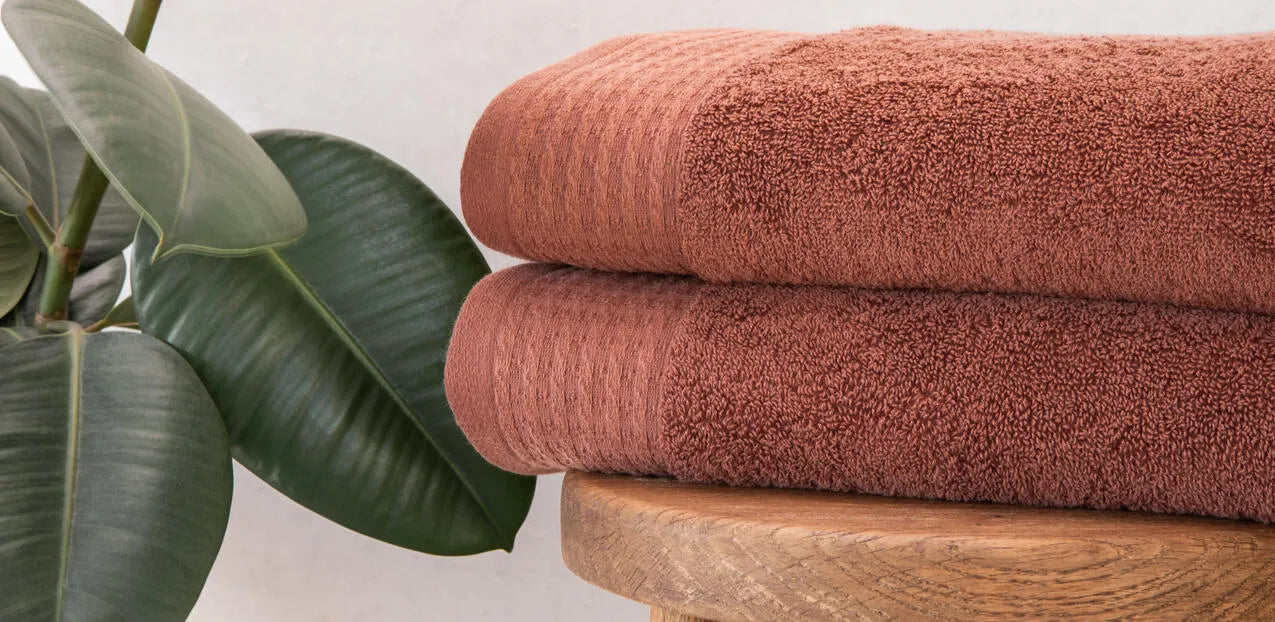 Twee Florence opgevouwen terracotta handdoeken op een houten kruk naast een groene kamerplant.